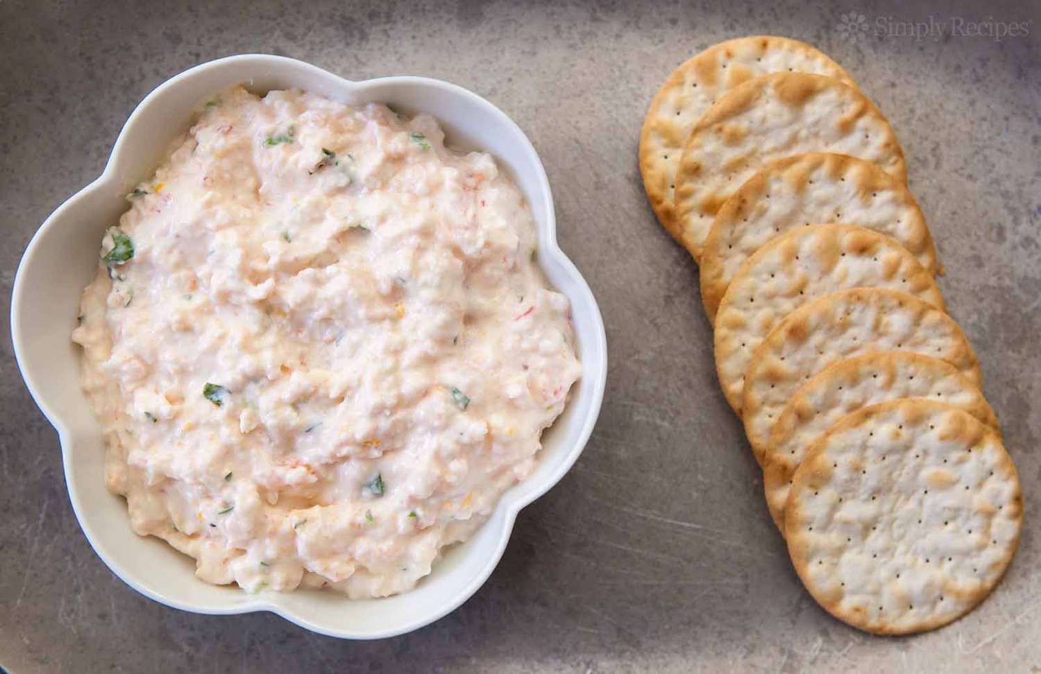 Shrimp dip in a bowl next to crackers arranged on a flat surface