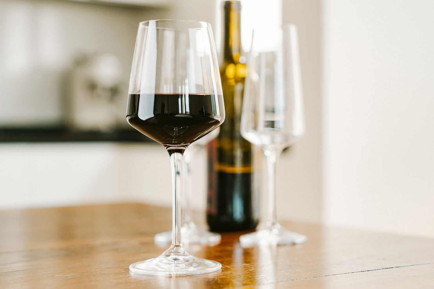Wine glass filled with red wine on a table with a wine bottle and empty glasses blurred in the background