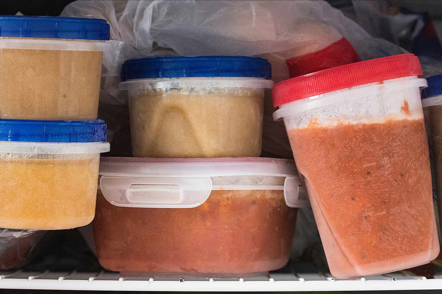 Containers of frozen food stored in a freezer varying types and portions in plastic containers with colored lids