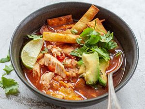 chicken tortilla soup served in a bowl with a spoon, topped with tortilla chips, lime, and cilantro