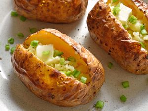 Baked potato on a plate topped with sliced onions and butter