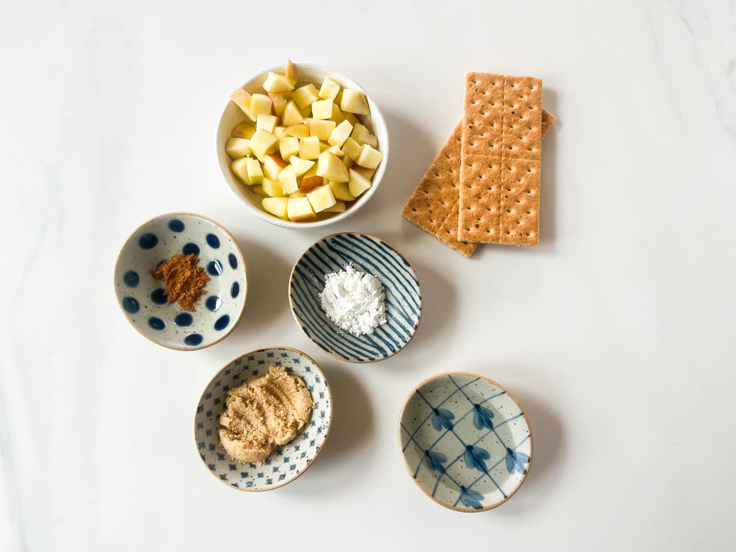 Cut apples graham crackers and small bowls of ingredients arranged for preparing a dish