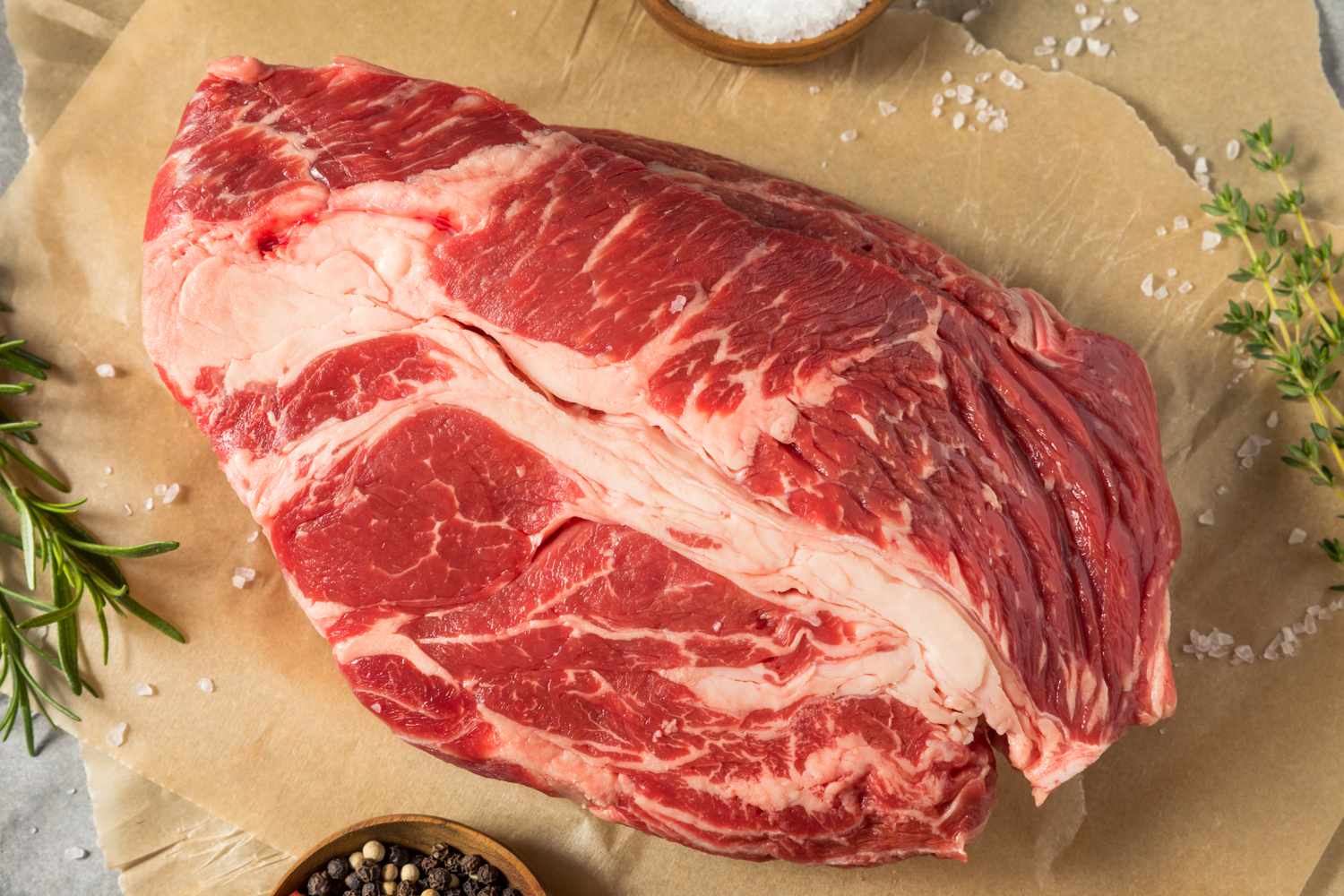 A raw cut of beef placed on parchment paper with salt and herbs beside