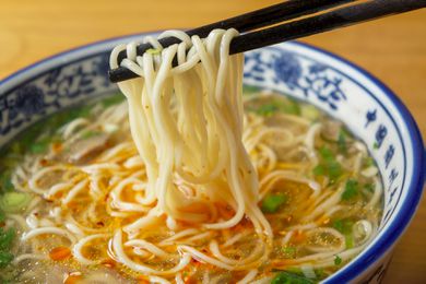 Chopsticks lifting ramen noodles from a bowl of soup with garnish