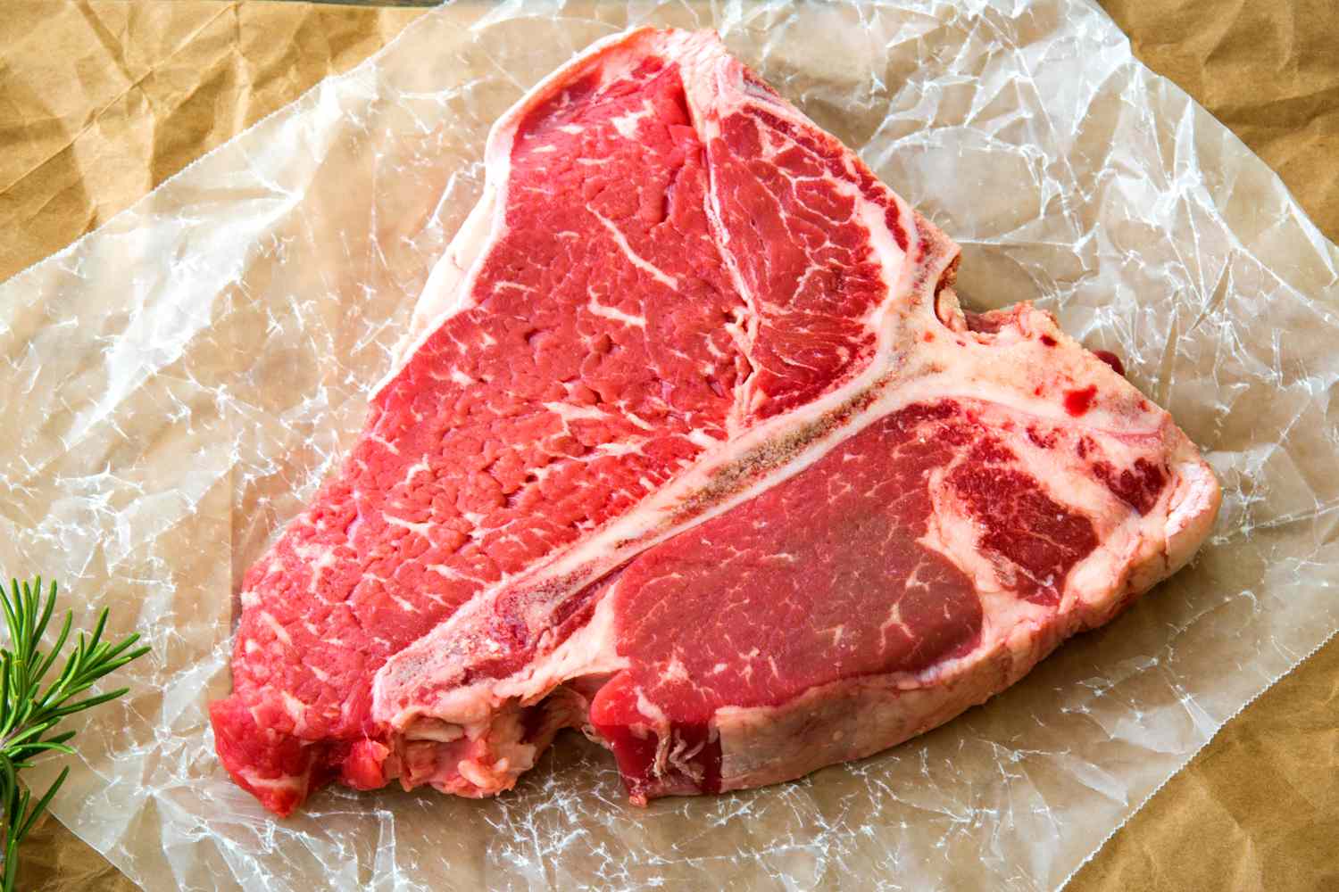 A raw Tbone steak placed on parchment paper garnished with a sprig of rosemary