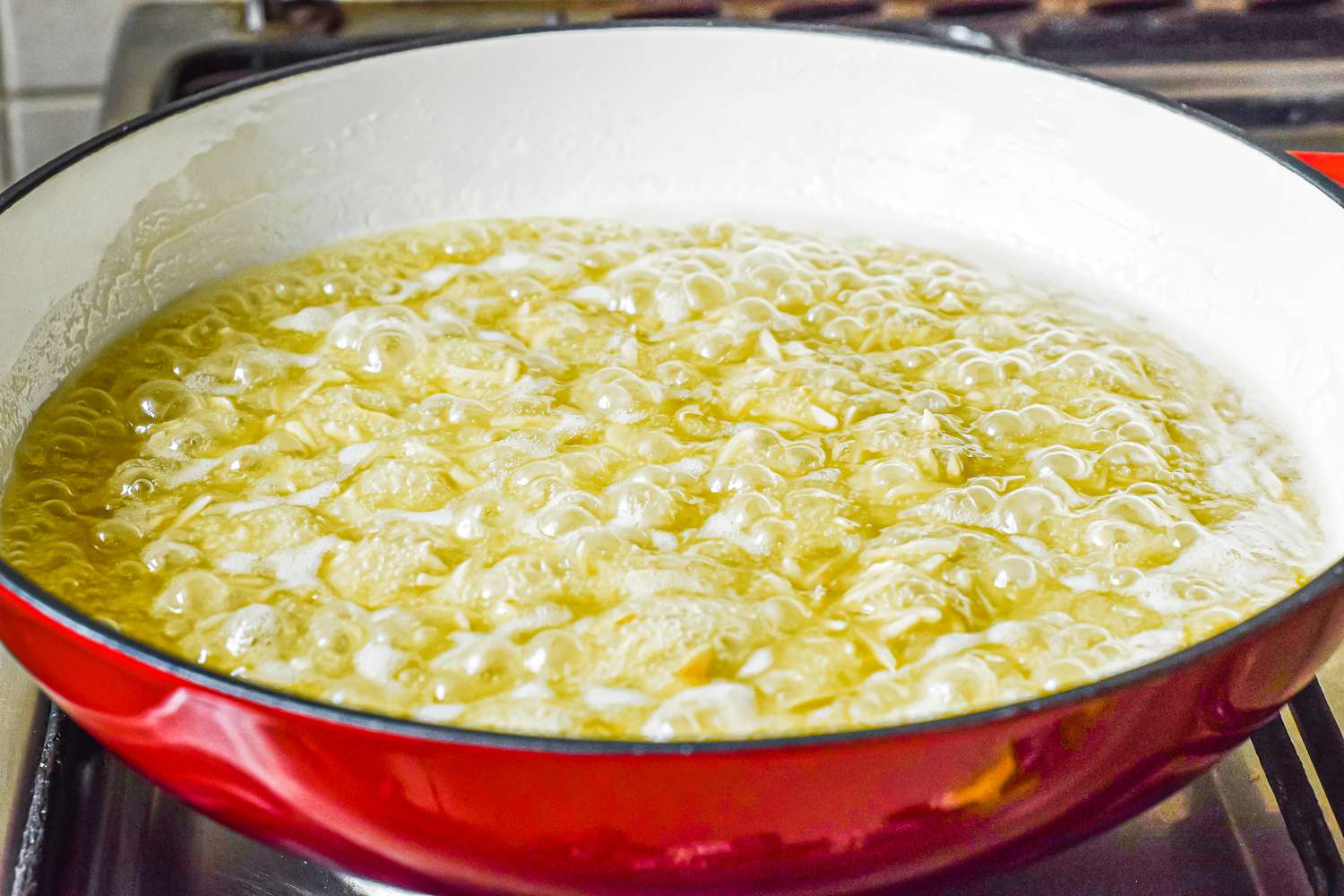 Butter and nuts simmering in a wide skillet to make Melting butter in a red pan to make an almond roca recipe.