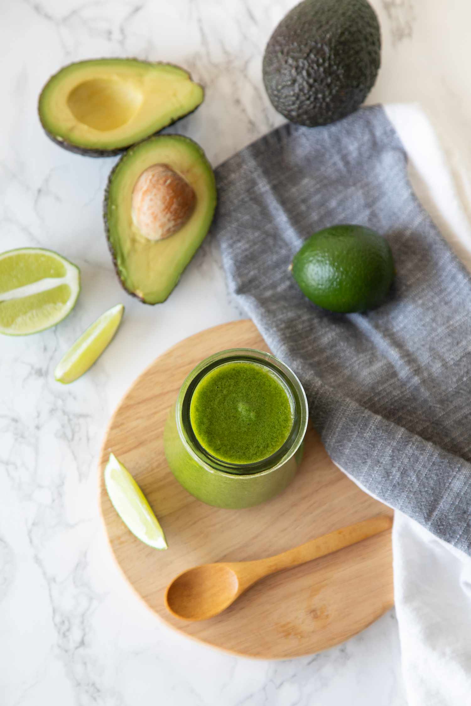 Avocado Lime Dressing on Wooden Tray Next to a Spoon, Limes, and Avocados