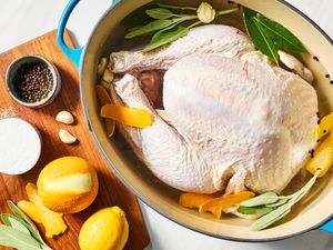A raw turkey in a pot with herbs, citrus, spices, and brine