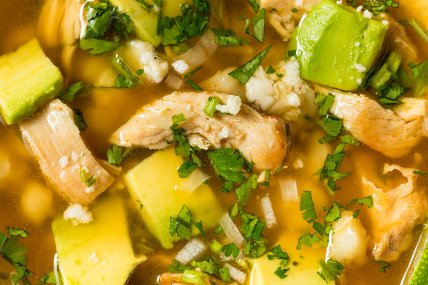 Bowl of posole topped with chunks of avocado shredded chicken and cilantro