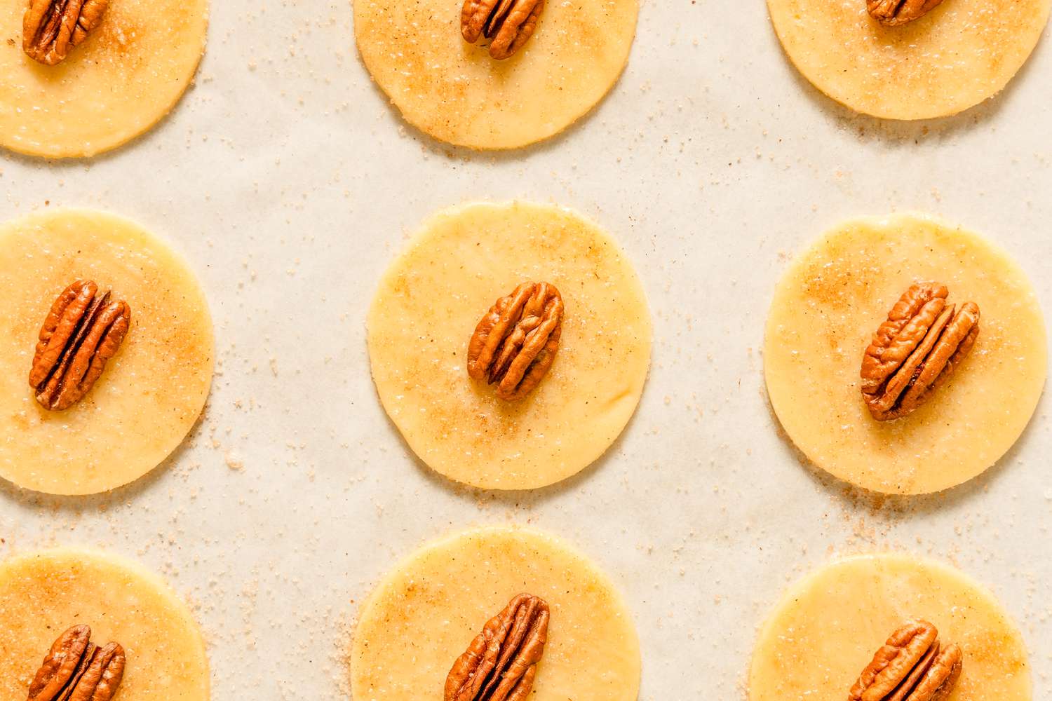 Closeup view of the cut out cookies brushed with egg white and topped with a pecan half and cinnamon sugar mixture for Sand Tarts recipe
