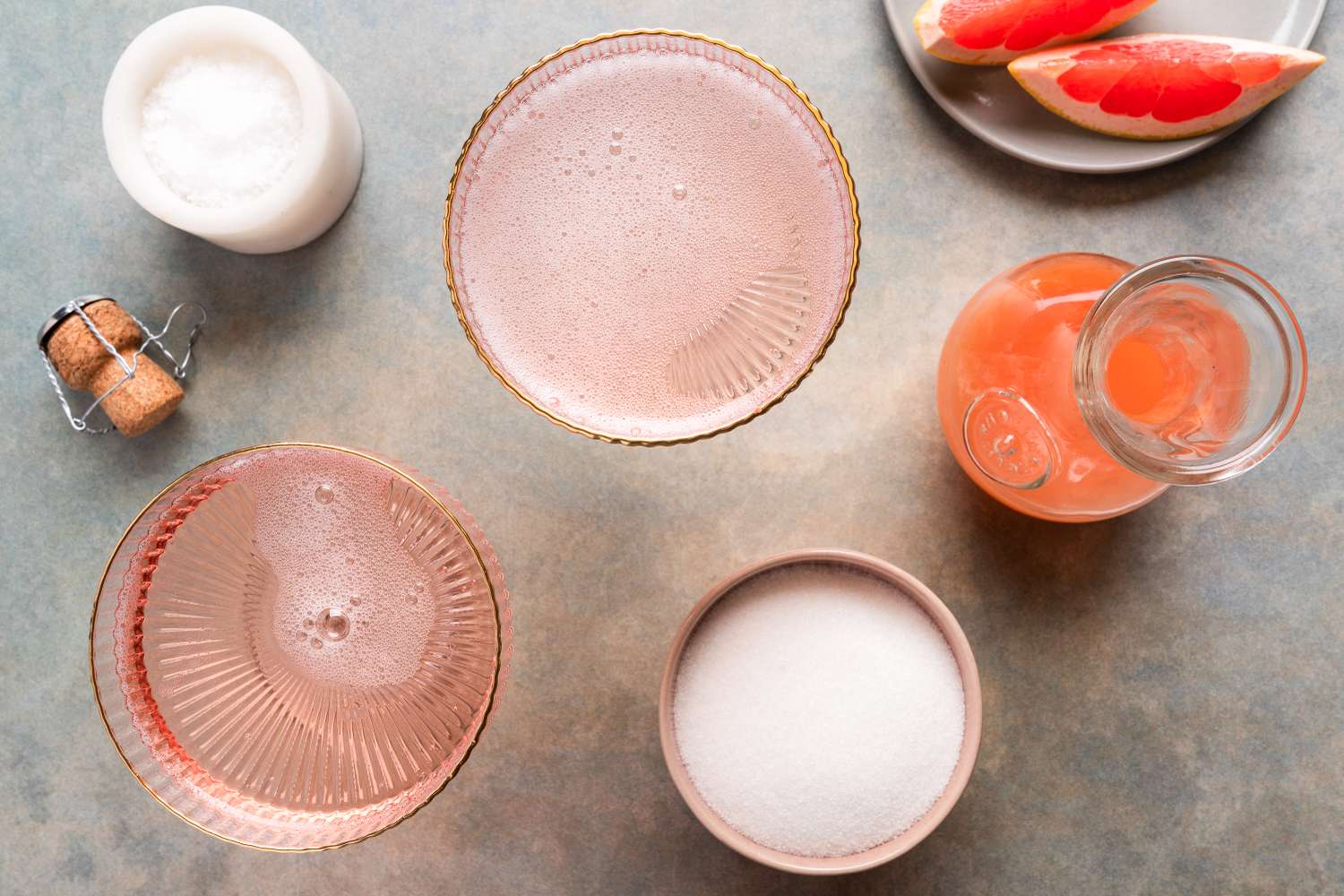 A prepared grapefruit granita with ingredients arranged including a beverage in glasses salt sugar a citrus drink and grapefruit slices