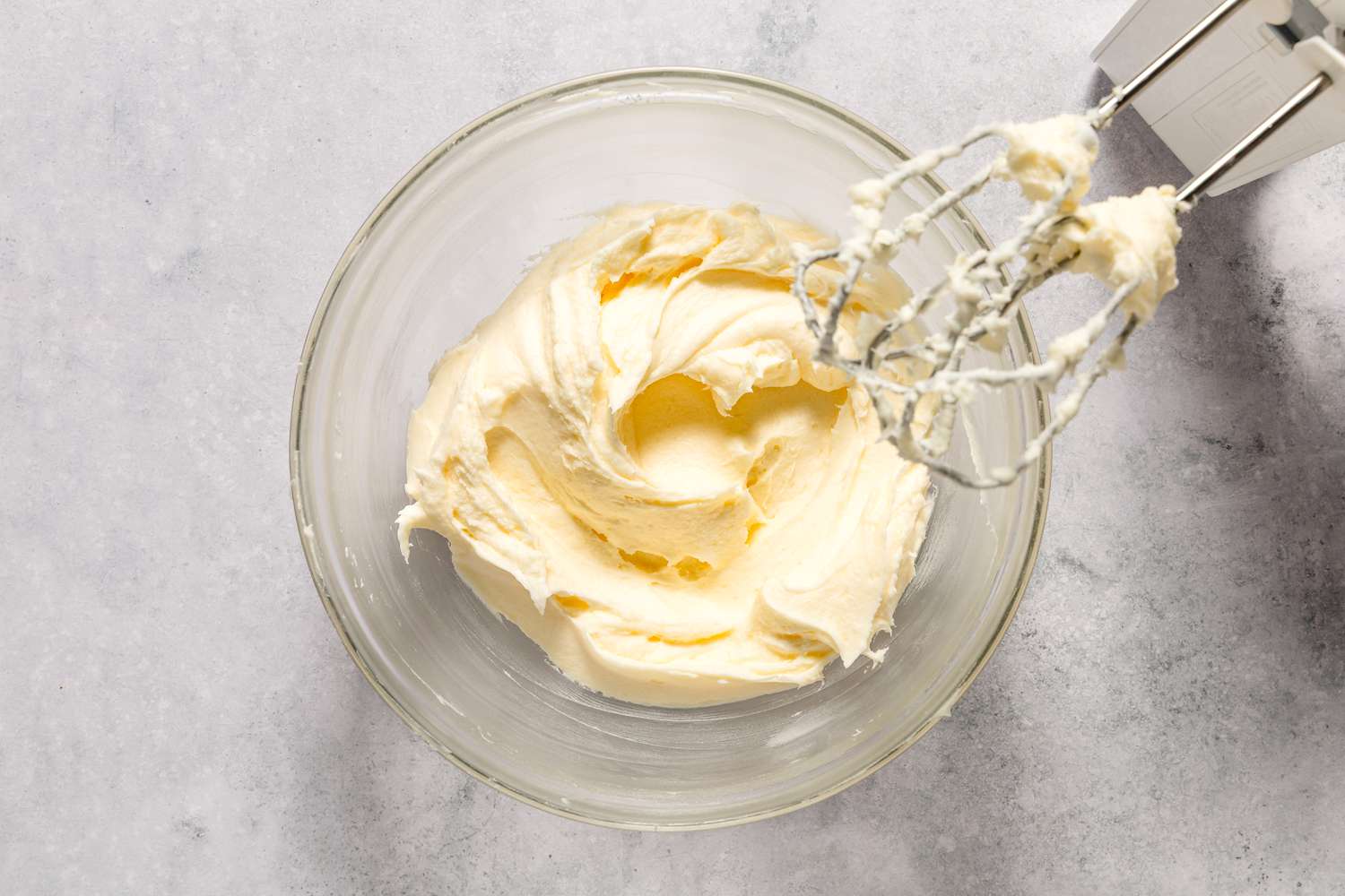 Bowl of creamed butter, cream cheese and sugar from Easy Carrot Cake recipe with a hand mixer attachment next to it.