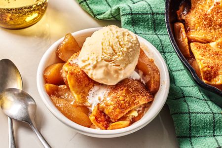 A white bowl with a serving of Apple Pandowdy topped with a scoop of vanilla ice cream