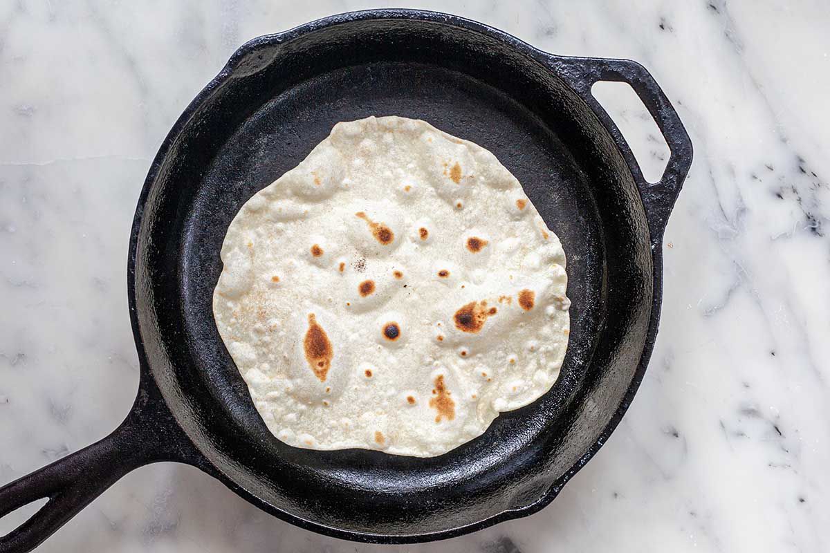 Flour tortilla cooking in a cast iron skillet on a marble countertop for a easy homemade flour tortilla.
