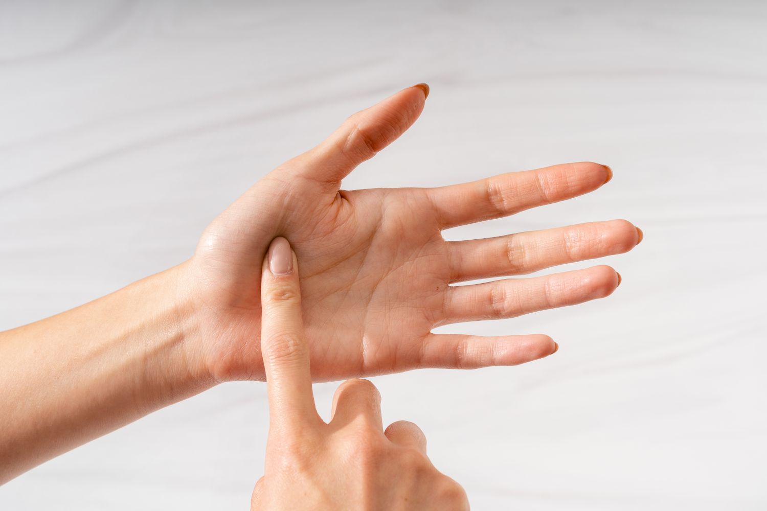 A finger touching the palm of an open hand to demonstrate the finger test for the doneness of cooked meat (raw)