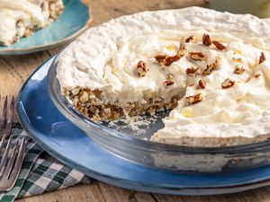 Angled view of a cream pie topped with pecans with a slice removed in a clear glass pie plate resting on a blue plate and a wooden tabletop