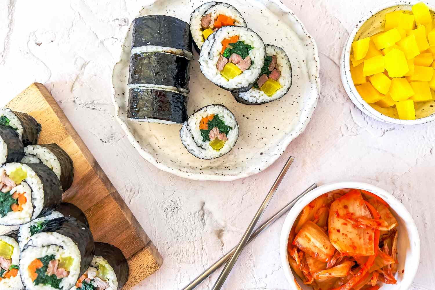 Classic Kimbap on a Plate and a Wooden Plaque Next to Two Bowl of Danmuji and Kimchi