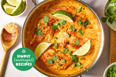 A pan of a cooked dish garnished with lime wedges herbs and sauce