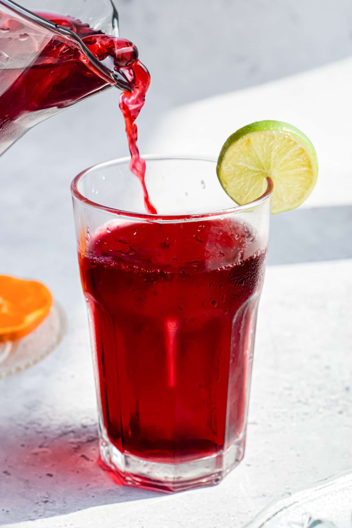 Agua de Jamaica (Hibiscus Tea) Poured From a Pitcher into a Glass of Ice with a Lime Slice