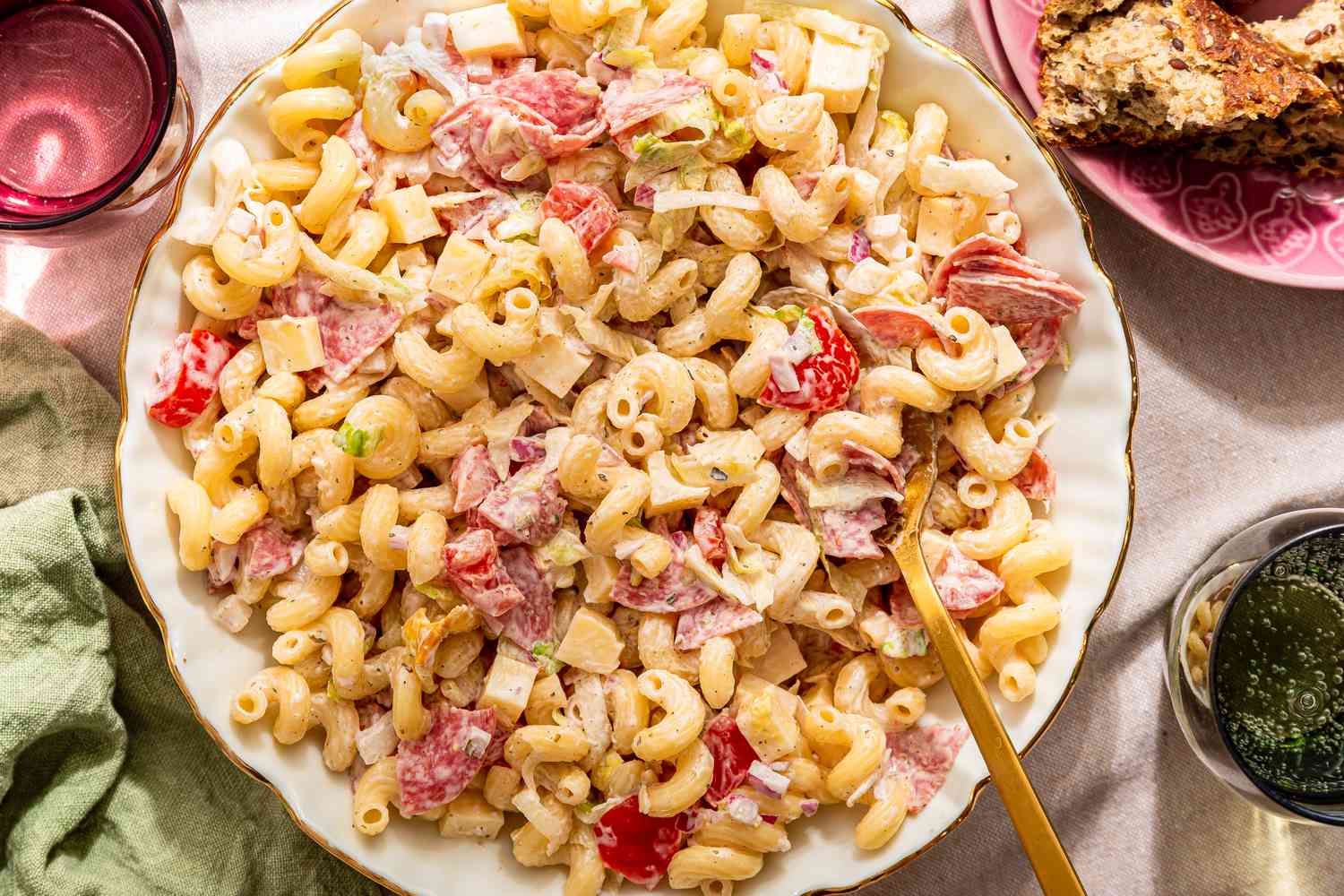 ginder pasta salad in a bowl with serving utensils at a table setting with glasses of water, a table napkin, and a stack of plates (close-up)