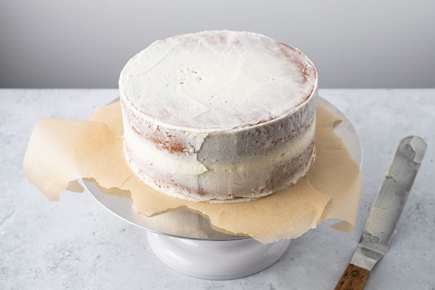 Lemon Lavender Cake with Crumb Coat Applied, Standing on a Cake Stand with Parchment Paper