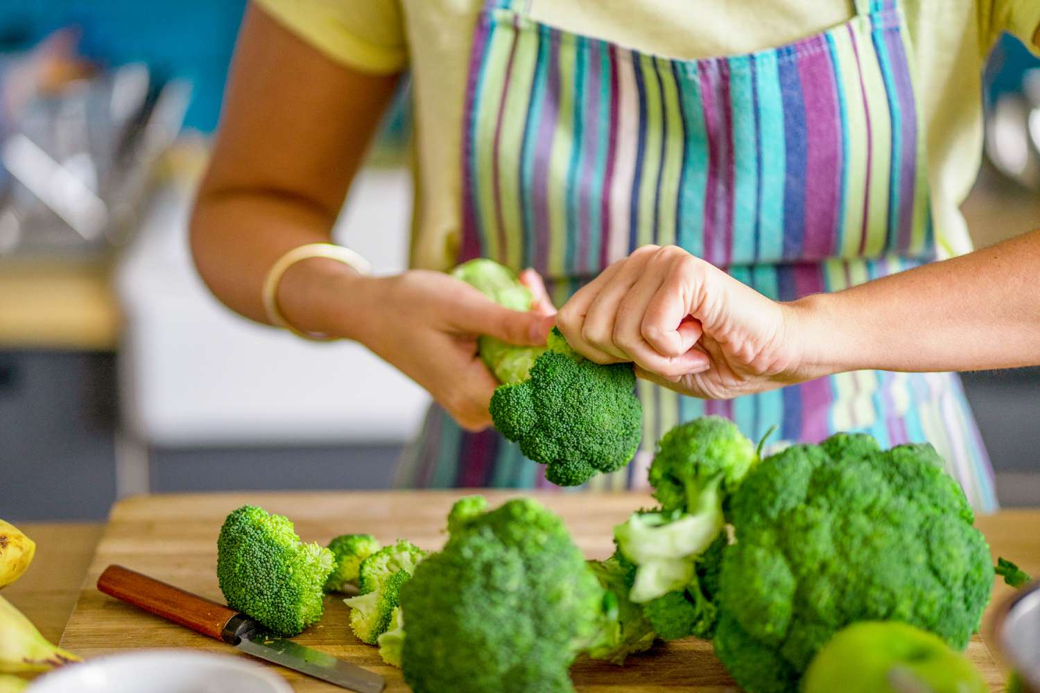 A person snapping off broccoli florrets from the stalk over a cutting board with more broccoli 