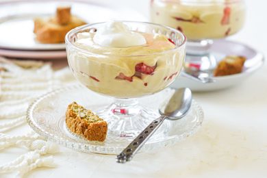 Two parfait glasses with a custard dessert topped with cream and layered with strawberries.