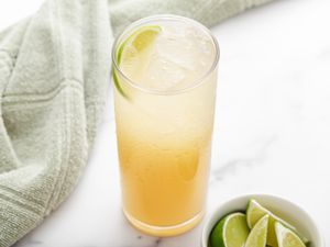 A tall glass of ginger ale soda with a bowl of sliced limes next to it.