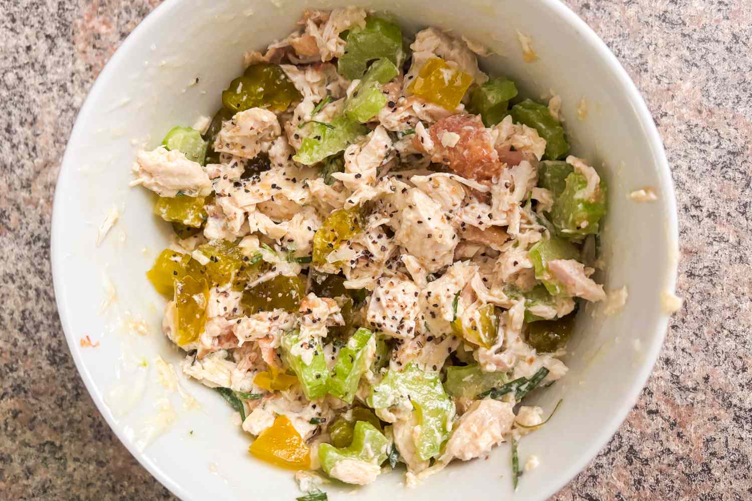 A bowl containing chicken salad mixed with vegetables and seasonings