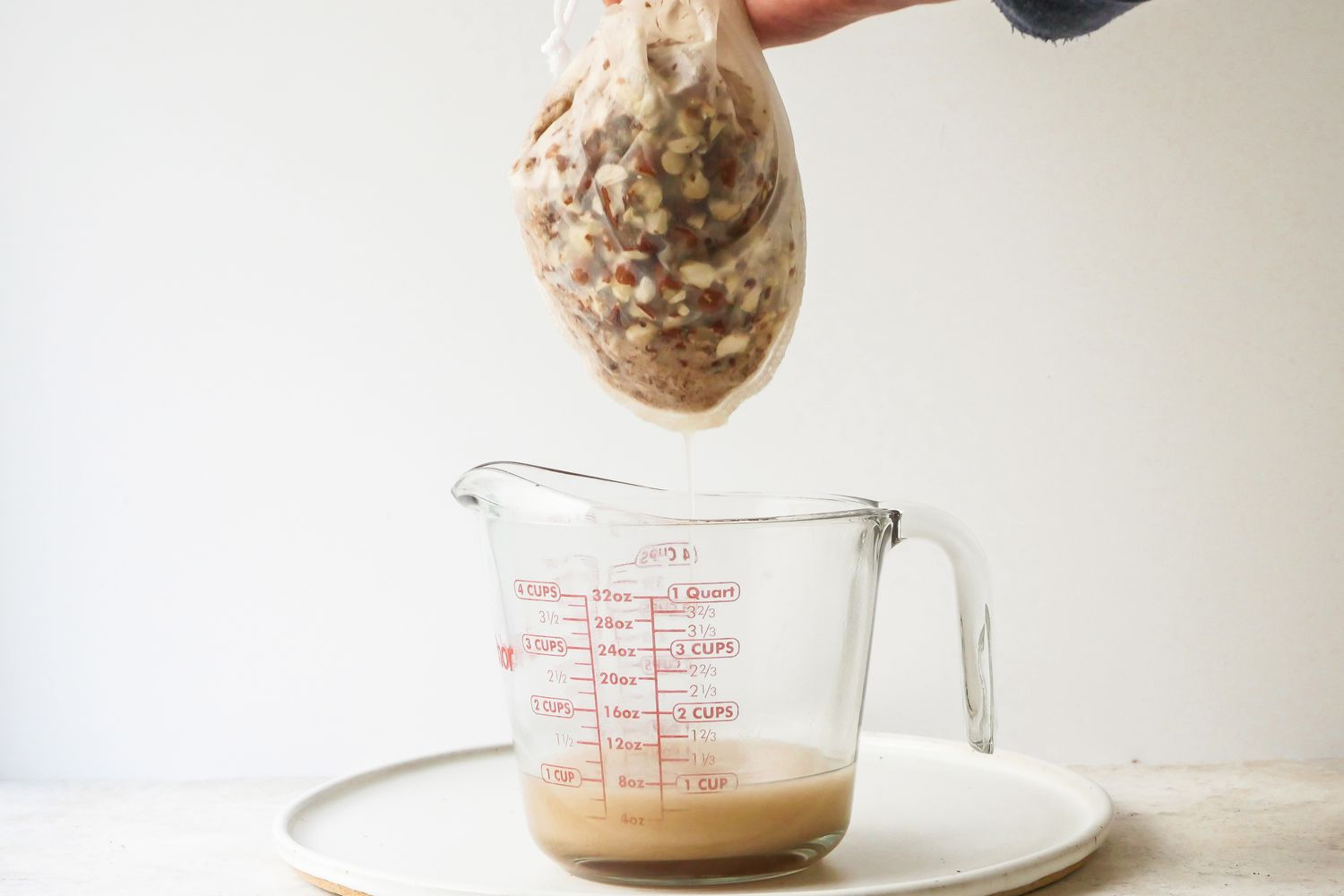Straining soaked almonds into a measuring cup for an Orgeat recipe.