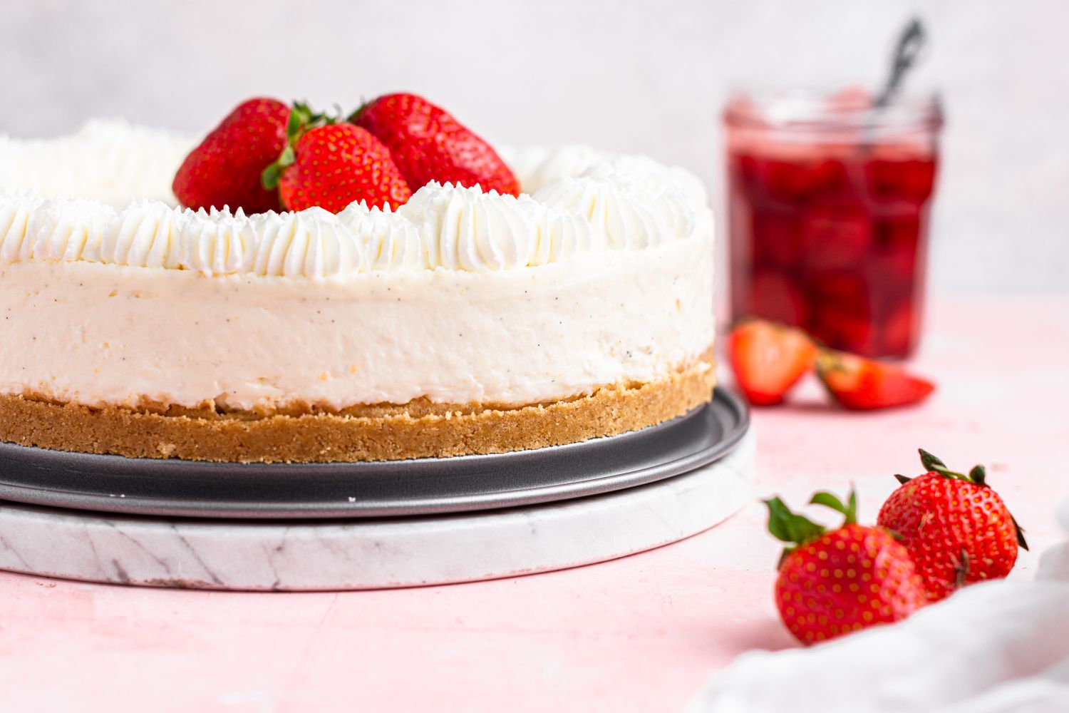 A whole easy no bake cheesecake topped with strawberries on a pink background.