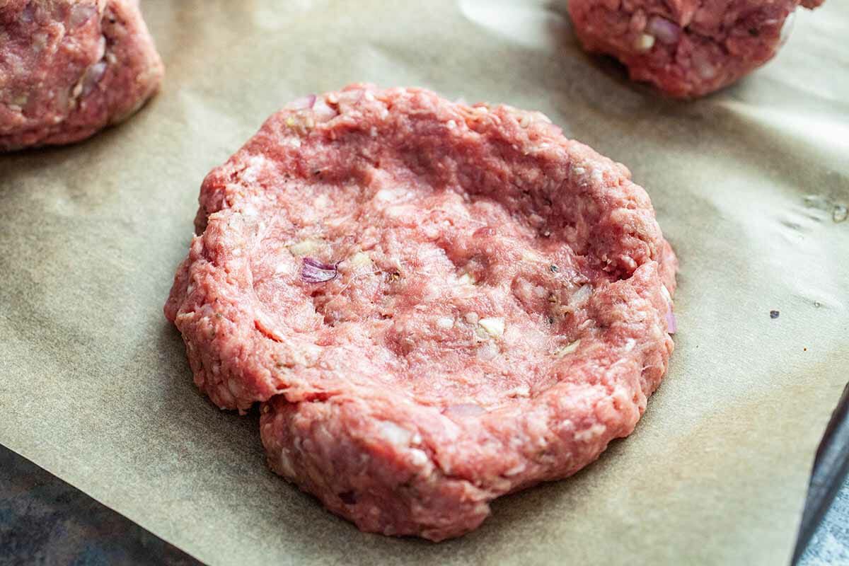 A flattened raw burger patty on a sheet of parchment paper