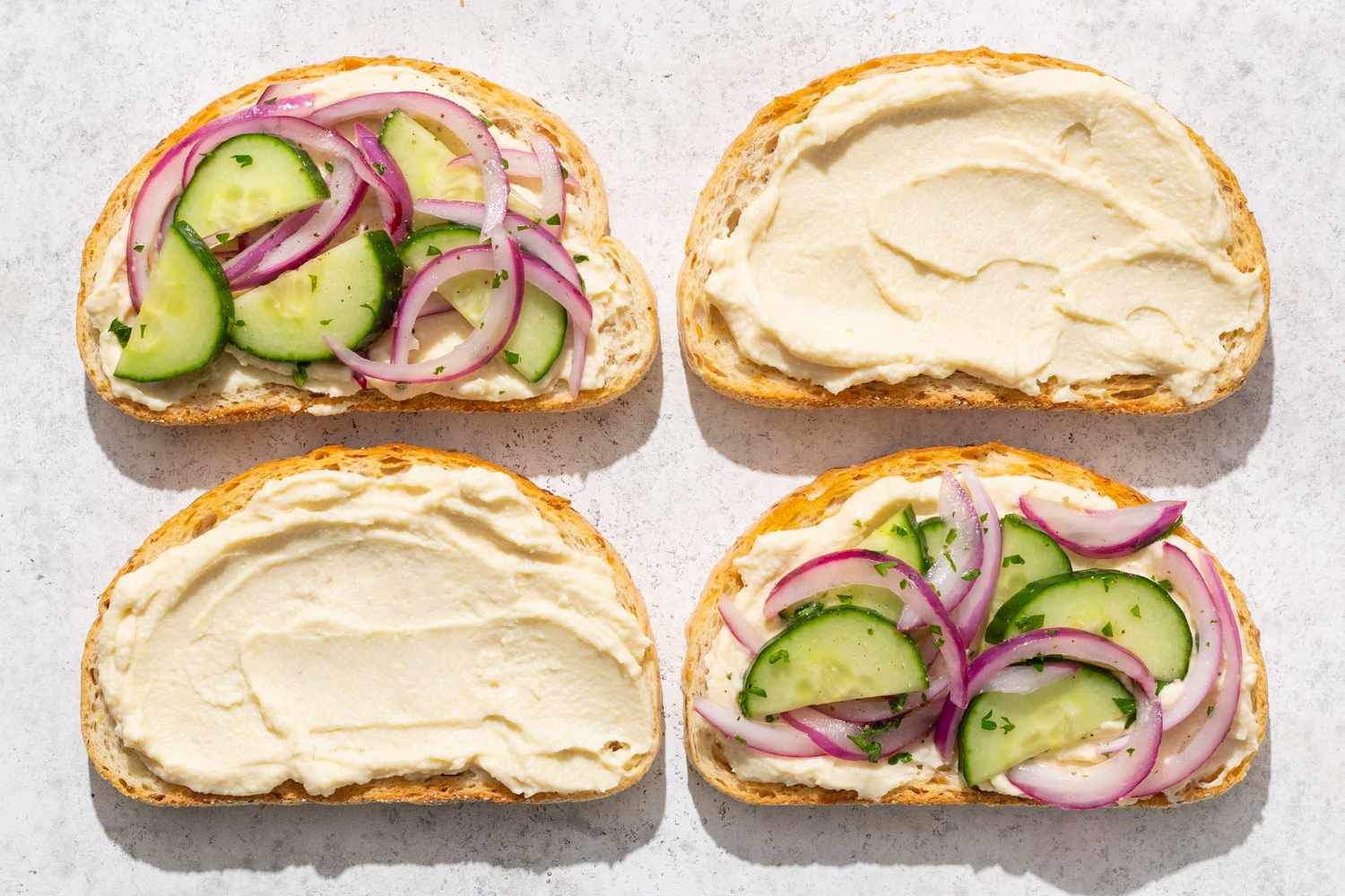 Four slices of bread with hummus cucumber and onion