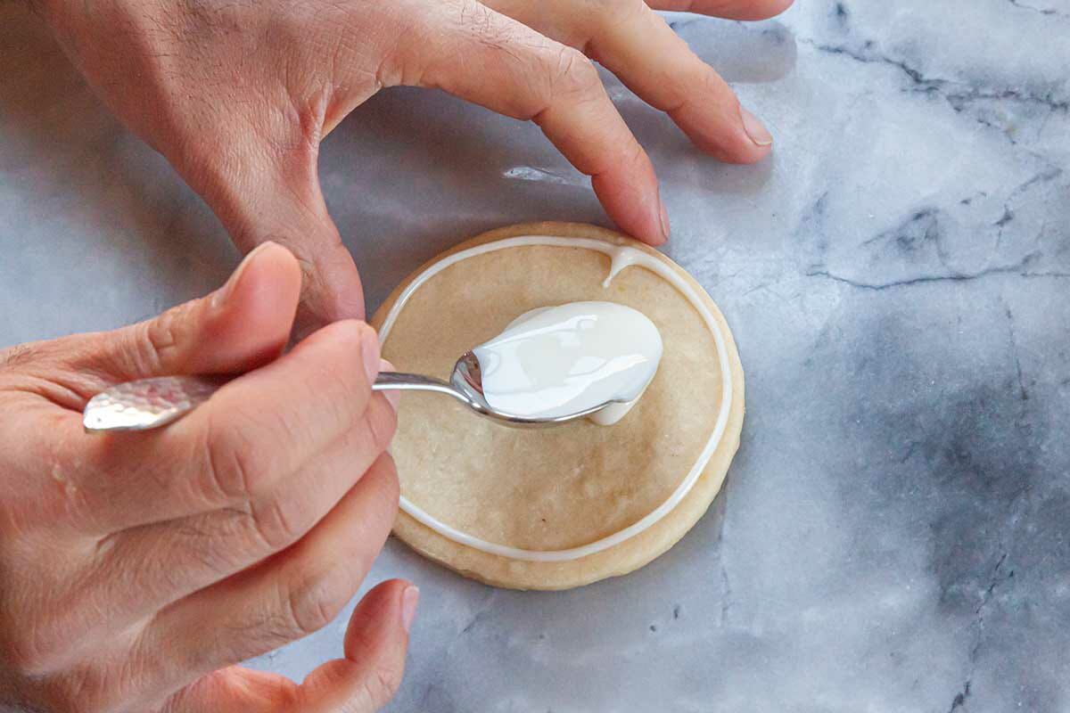 Spooning white royal icing on a sugar cookie.