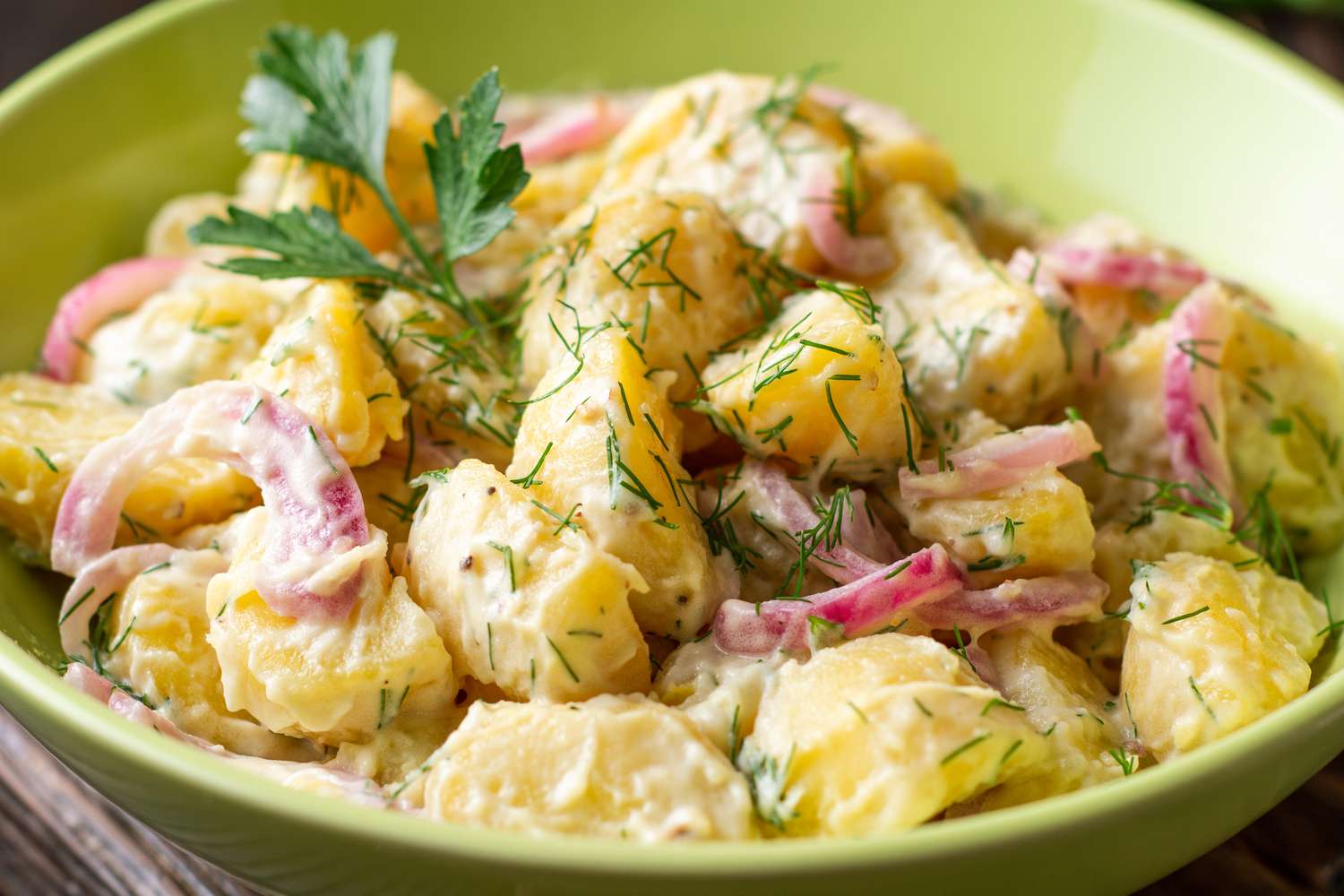 potato salad in a bowl topped with dill and parsley
