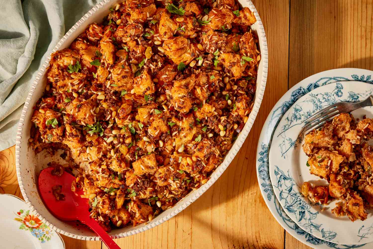 A oval white serving dish with Greek-style stuffing, with a portion scooped out and placed on a plate next to the serving dish