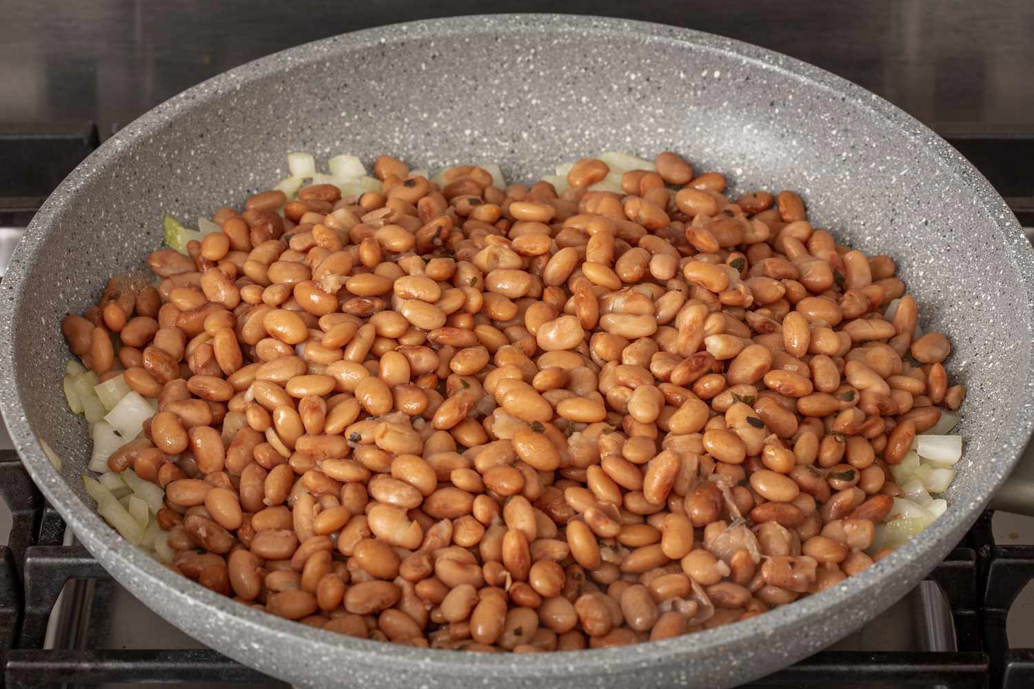 Beans and onions in a skillet to make refried beans recipe.