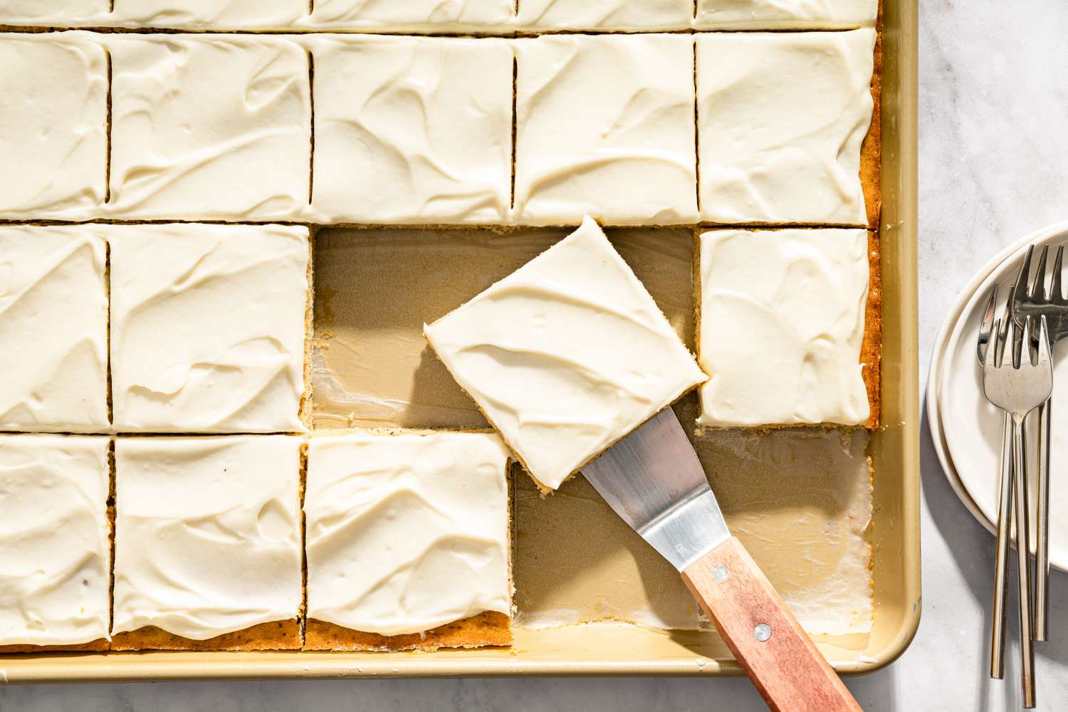 Sliced frosted dessert bars on a sheet pan with one piece lifted on a spatula