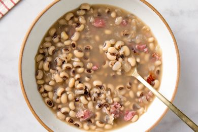 A bowl of cooked blackeyed peas in broth with pieces of meat and a spoon