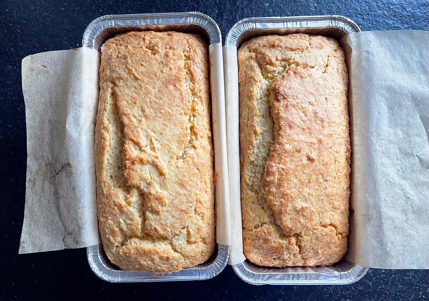 Two loaves of cornbread in baking pans on a dark surface
