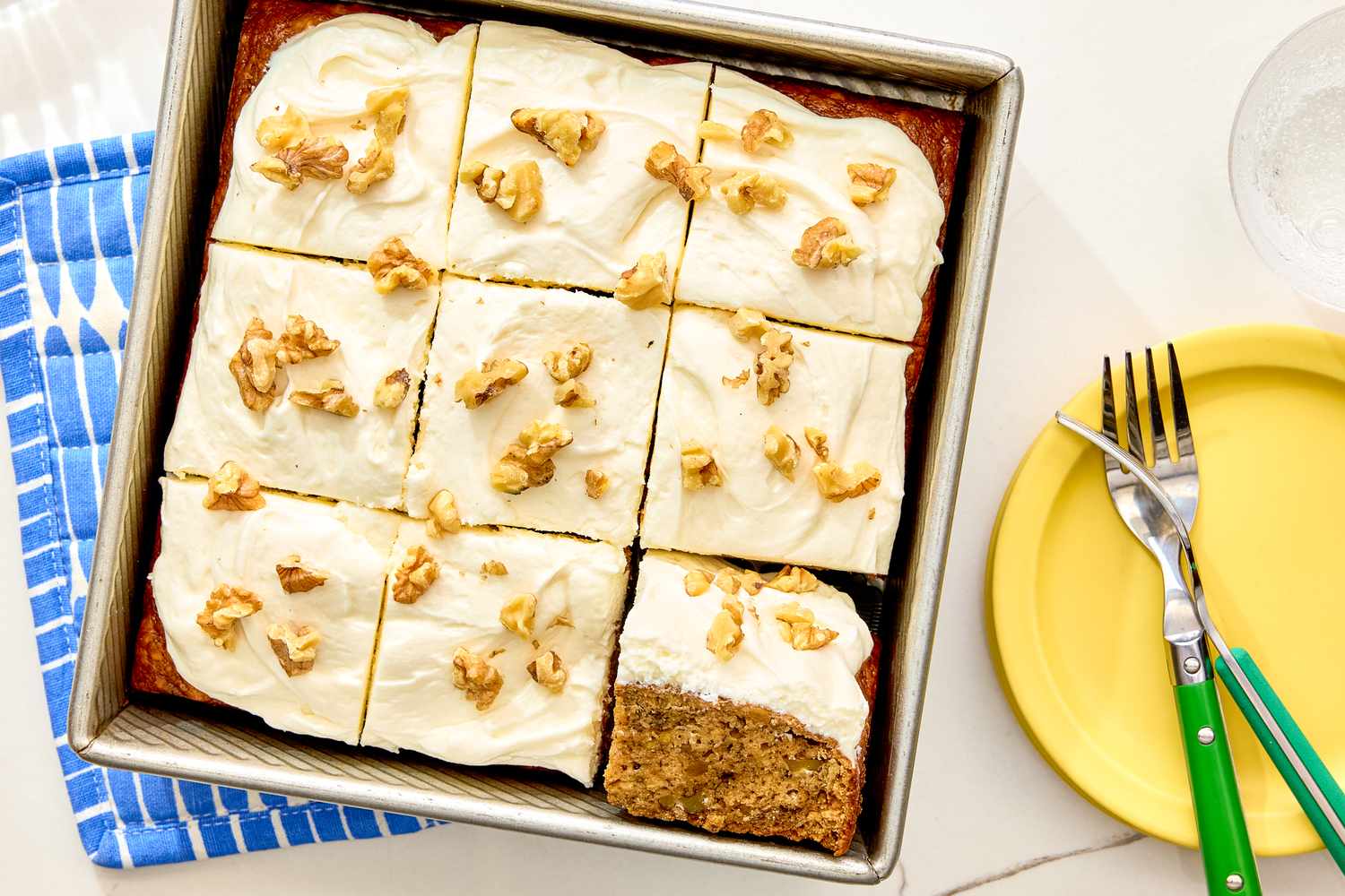 Banana bread cake with frosting and walnuts cut into squares in a baking pan