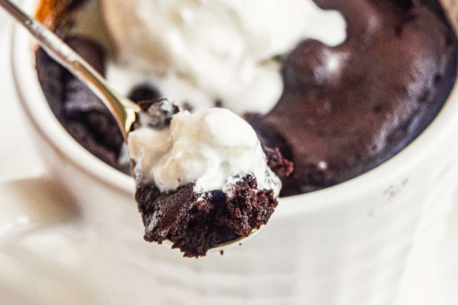 A spoonful of brownie with whipped cream taken from a mug dessert