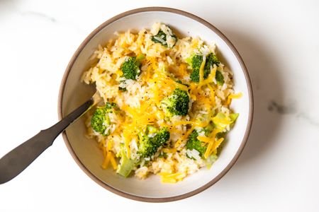 A bowl of rice mixed with broccoli and topped with melted cheese a spoon on the side