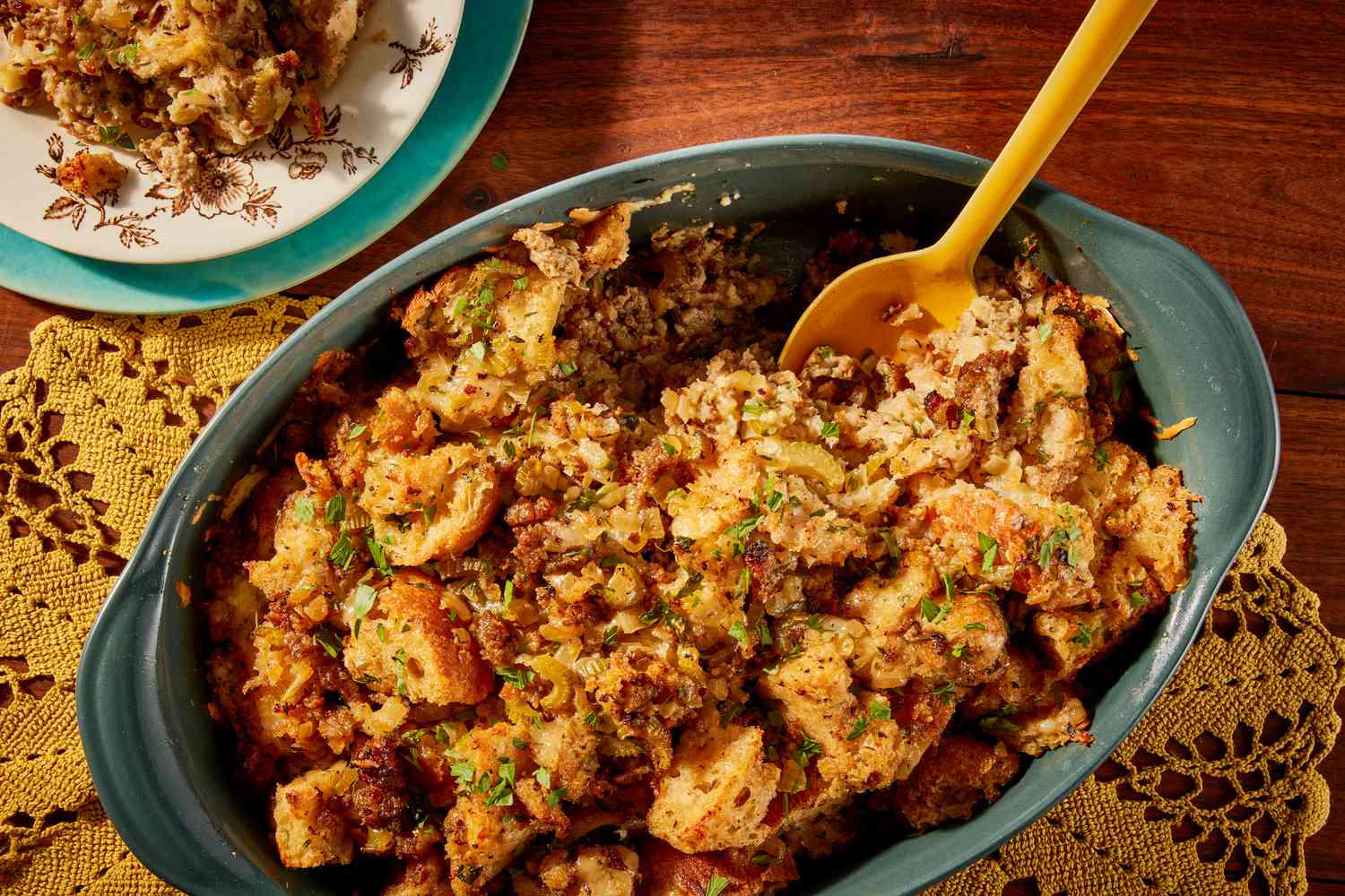 Overhead view of a green casserole dish of Wisconsin-style stuffing with a serving spoon over a yellow doily on a wooden tabletop