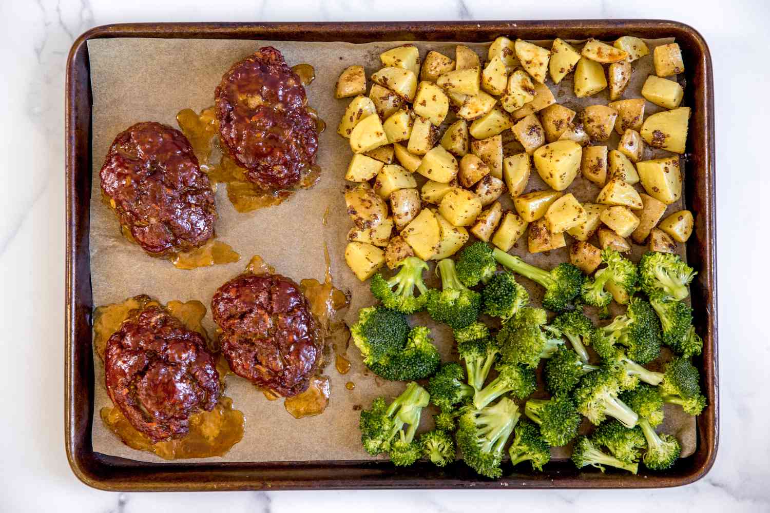 Overhead view of a sheet pan of mini meatloaves with veg and potatoes in a sheet pan.