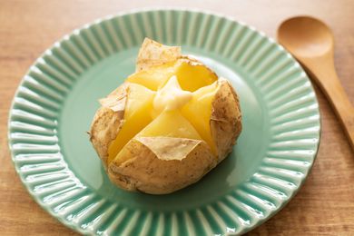 A green plate with a baked potato, topped with a click of butter