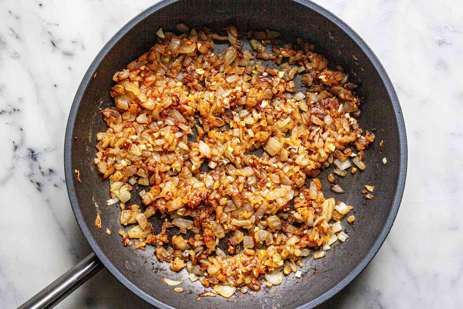 Aromatics cooked in a skillet to show how to make smothered chicken thighs in onion gravy