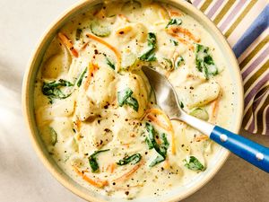 A bowl of creamy gnocchi soup with vegetables garnished with spinach and served with a spoon