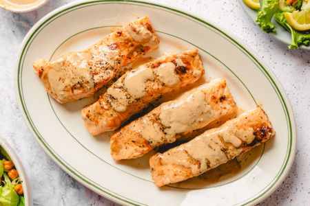 Four salmon fillets garnished with sauce on an oval plate