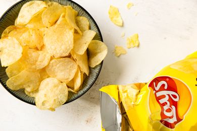 A bowl of potato chips next to an open bag of Lays chips chips scattered nearby